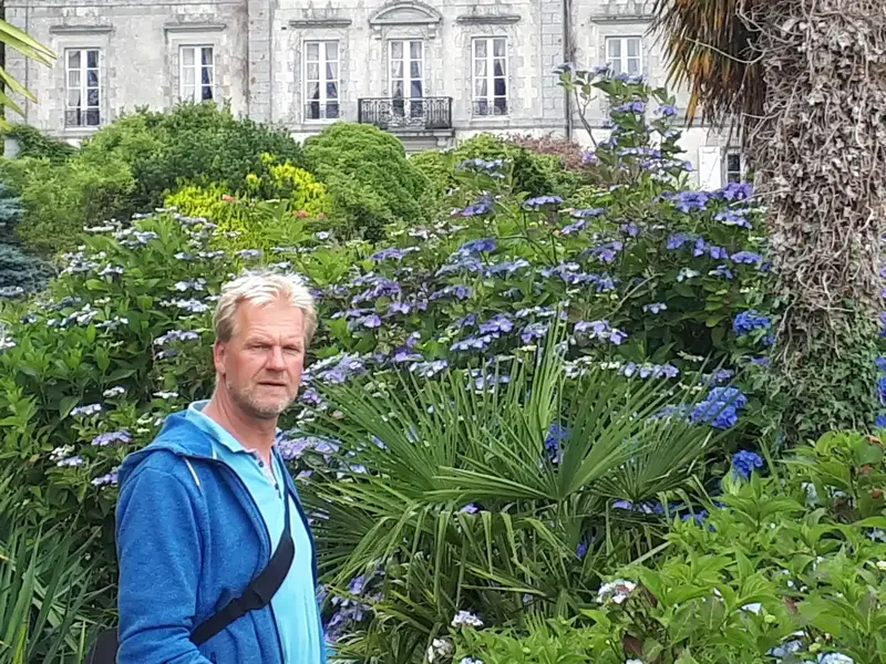 Foto: Der Baumsachverständige Marc Wilde Marc Wilde in einer wundervoll angelegten grünen Gartenanlage mit Sträuchern,
Pflanzen,
Bäumen,
im Hintergrund ein Herrenhaus